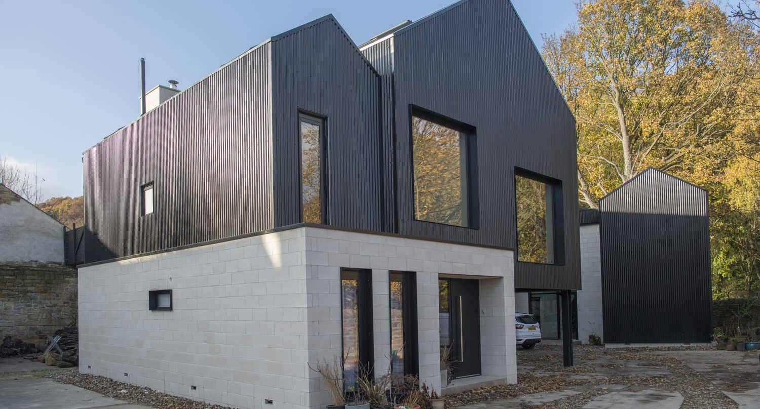 A modern house with a white brick ground floor and black upper floor featuring large windows and sleek sliding doors, set outdoors with trees in the background and a clear sky.