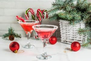 Christmas drinks, pink peppermint martini cocktail with xmas decoration and candy cane sweet on white marble kitchen table