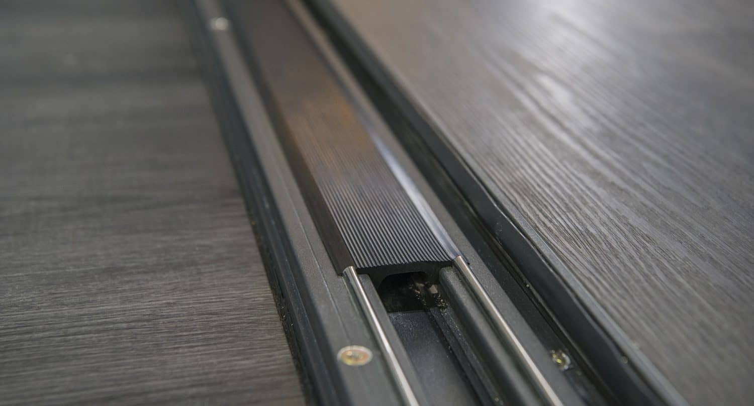 Close-up of a sliding door track with metal rails and a black grooved center on a dark wooden floor, ideal for modern sliding doors.