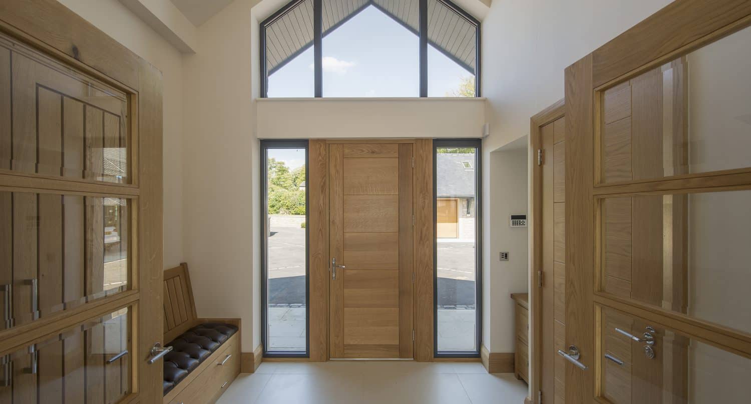 A modern entryway with a tall wooden front door flanked by glass panels, high ceiling, large window above the door, and stylish wooden cabinets with glass panels and a cushioned bench on the left highlights elegant front doors design.