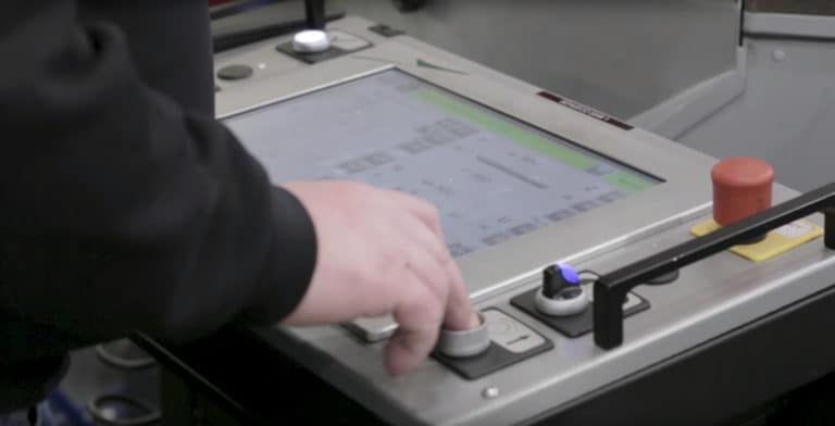 A person’s hand operates a large touchscreen control panel with various buttons, switches, and dials, suggesting the control of bespoke glass solutions or other advanced industrial equipment.