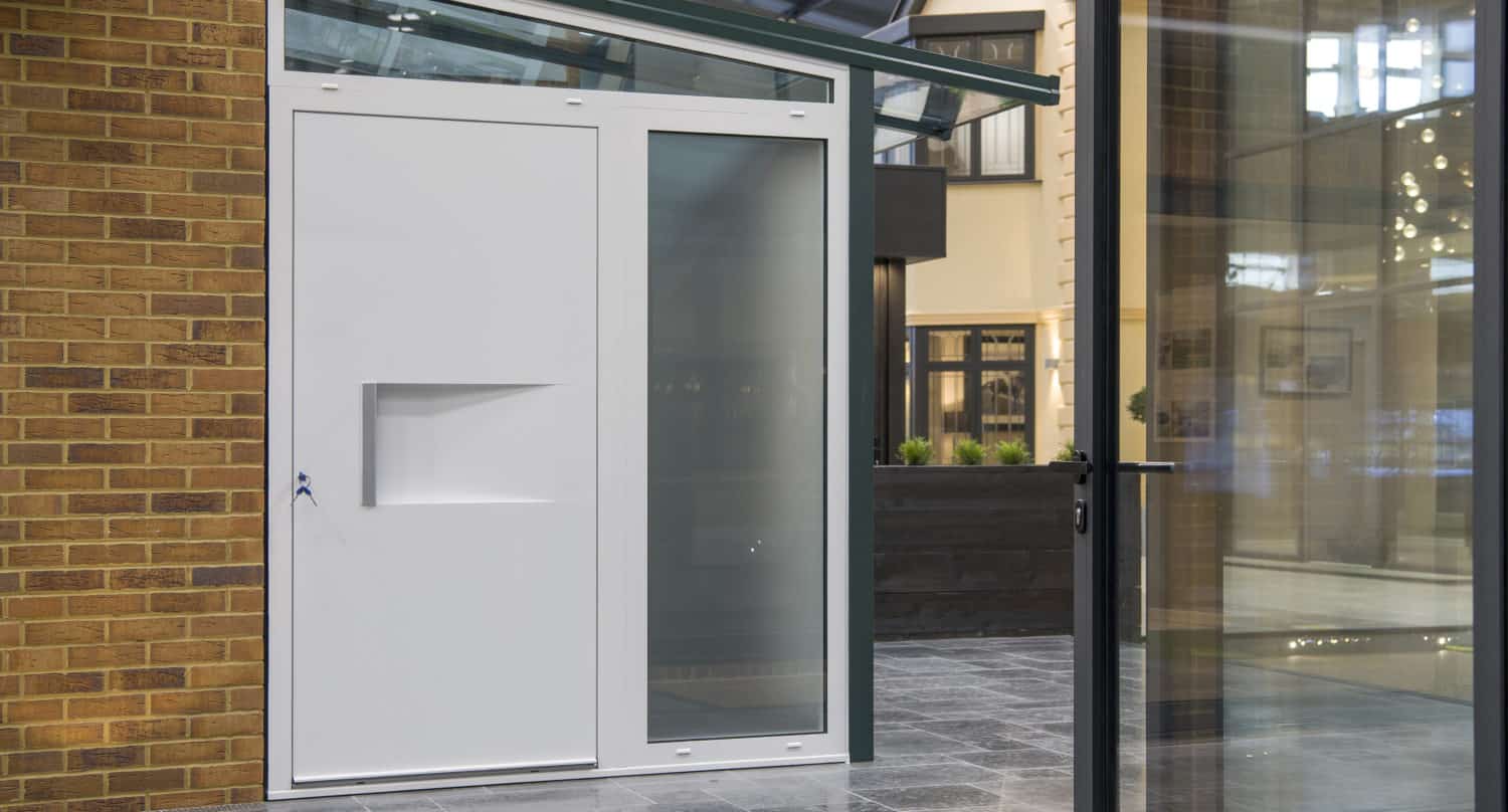 Modern white door with a rectangular handle and frosted glass panel, set in a metal frame next to bifold doors and a glass entryway in a contemporary building interior.