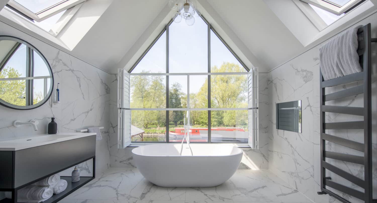 Modern bathroom with bespoke aluminium curtain walling illuminating a freestanding bath