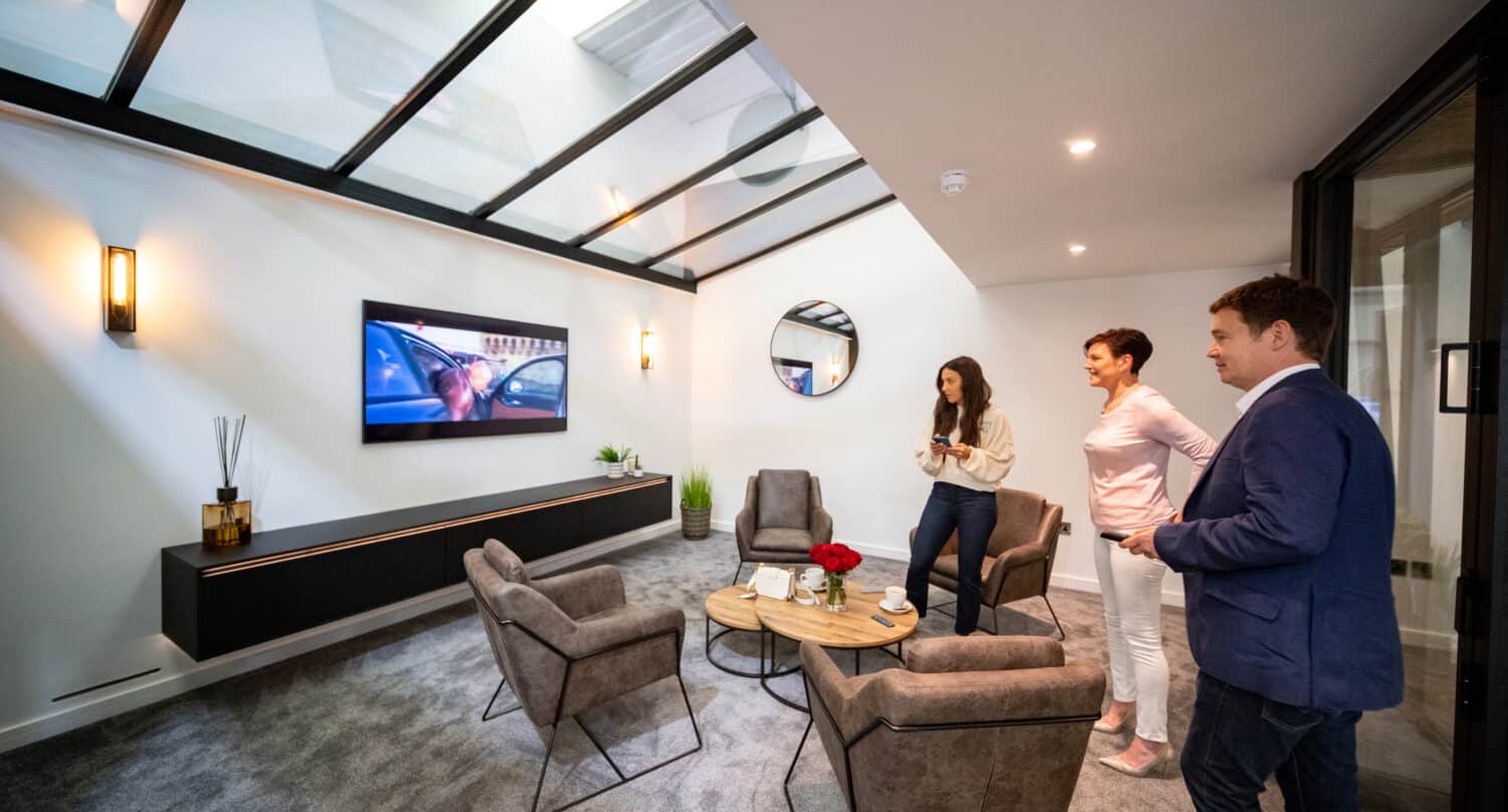Three people watching TV in a modern living room space featuring a glass roof