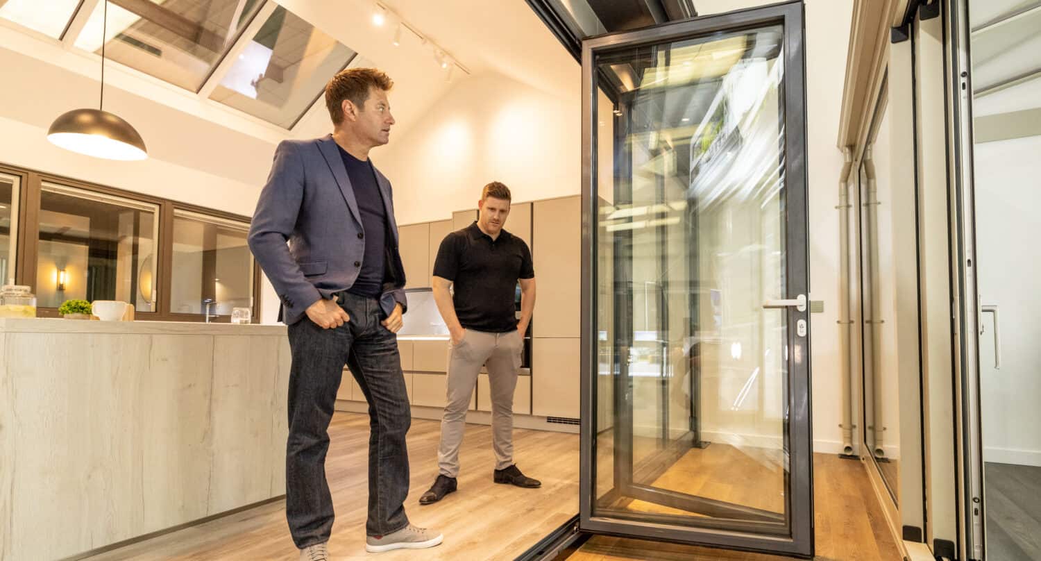 Two men in a modern kitchen looking to a 4 panel bifold doors in a showroom