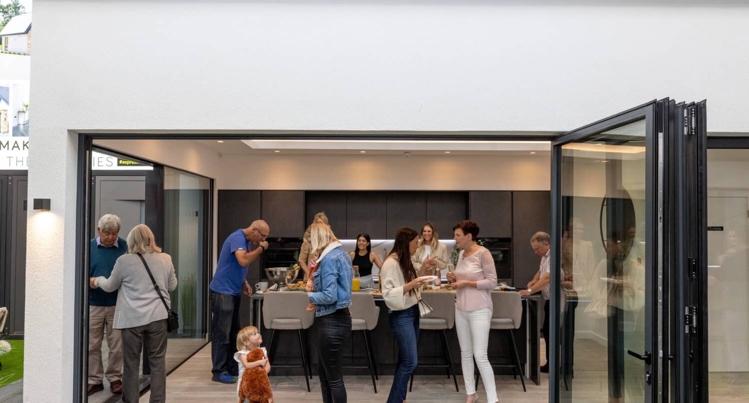 A group of people having a party in a modern kitchen that features black bifolding doors in a showroom