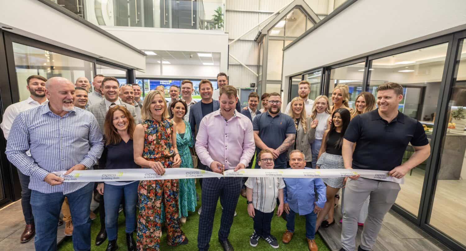 A man cutting a Express Bifolds tape in their showroom with a crowd behind