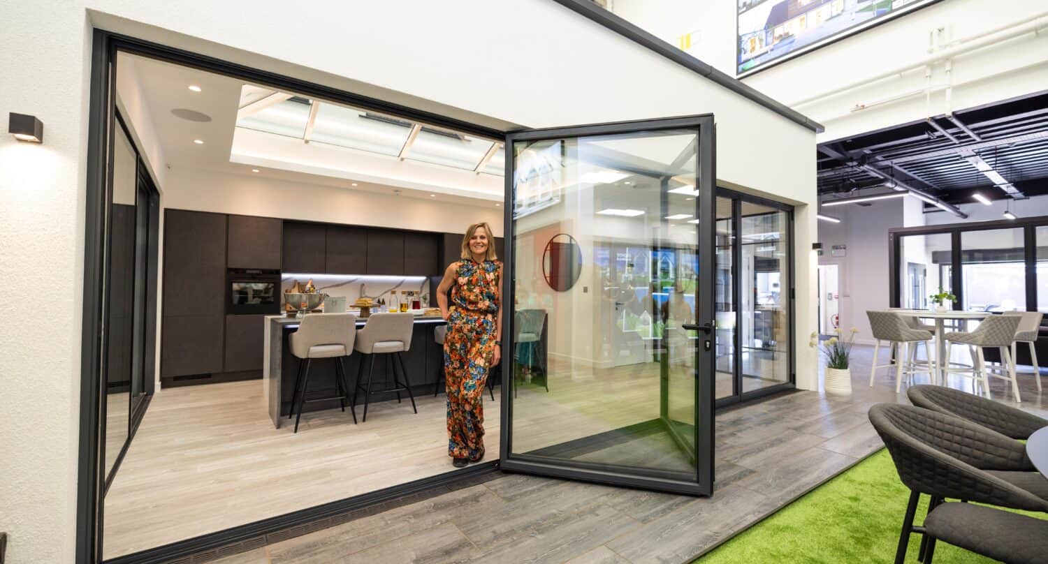 A woman posing in a modern kitchen that's featuring some large bifold doors in a showroom