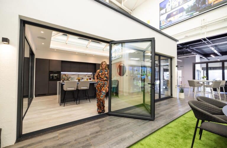 A woman posing in a modern kitchen that's featuring some large bifold doors in a showroom