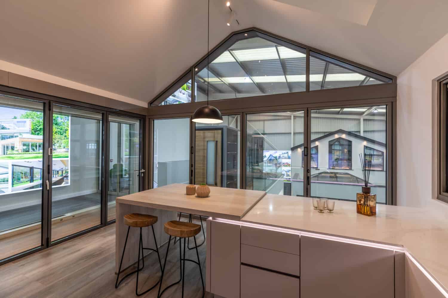 Modern clear kitchen featuring wide aluminium bi folding doors and shaped windows in a showroom