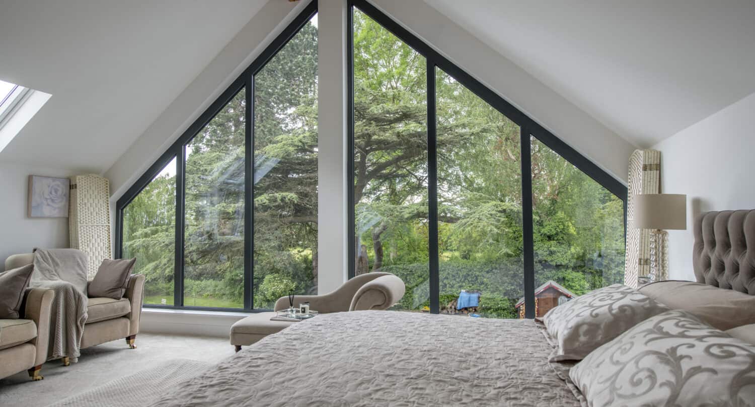 Modern master bedroom featuring two grey shaped aluminium windows with three panels each