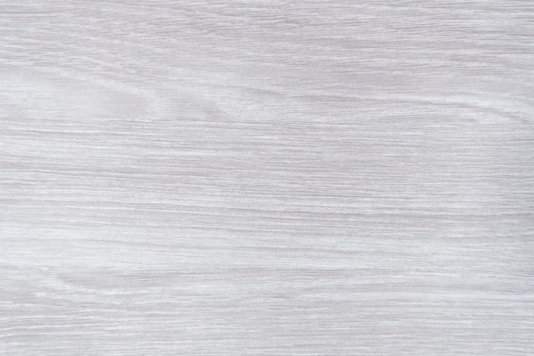 Light-colored wooden surface with a smooth texture and subtle, horizontal wood grain patterns, perfect for complementing bifold doors or bespoke glass solutions. The wood features soft shades of gray and white throughout.
