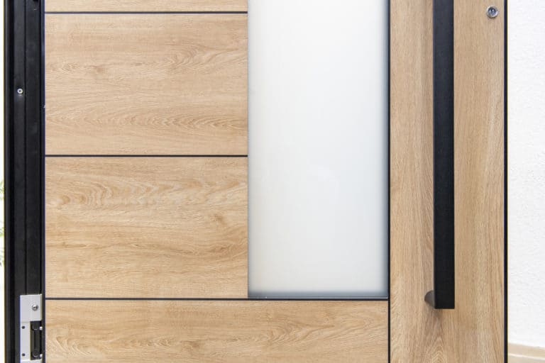 Close-up of a modern wooden front door with horizontal panels, a frosted glass section, and a vertical black handle. The design is minimalist and contemporary, showcasing bespoke glass solutions for a stylish entrance.