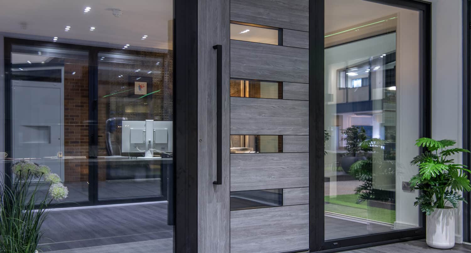 Modern glass and wood front door with horizontal panels and a large black handle, flanked by glass side panels. Indoor plants add freshness, while the space features a contemporary, clean design ideal for stylish front doors.