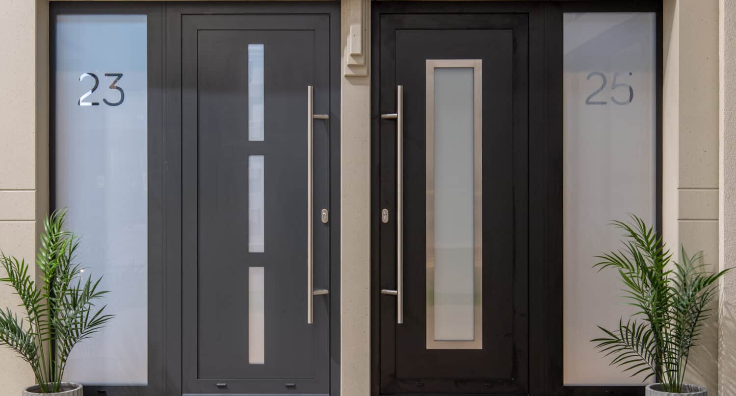 Two modern front doors side by side, one dark gray with the number 23 and one black with the number 25, each flanked by frosted glass panels and potted green plants—sleek style for contemporary front doors.