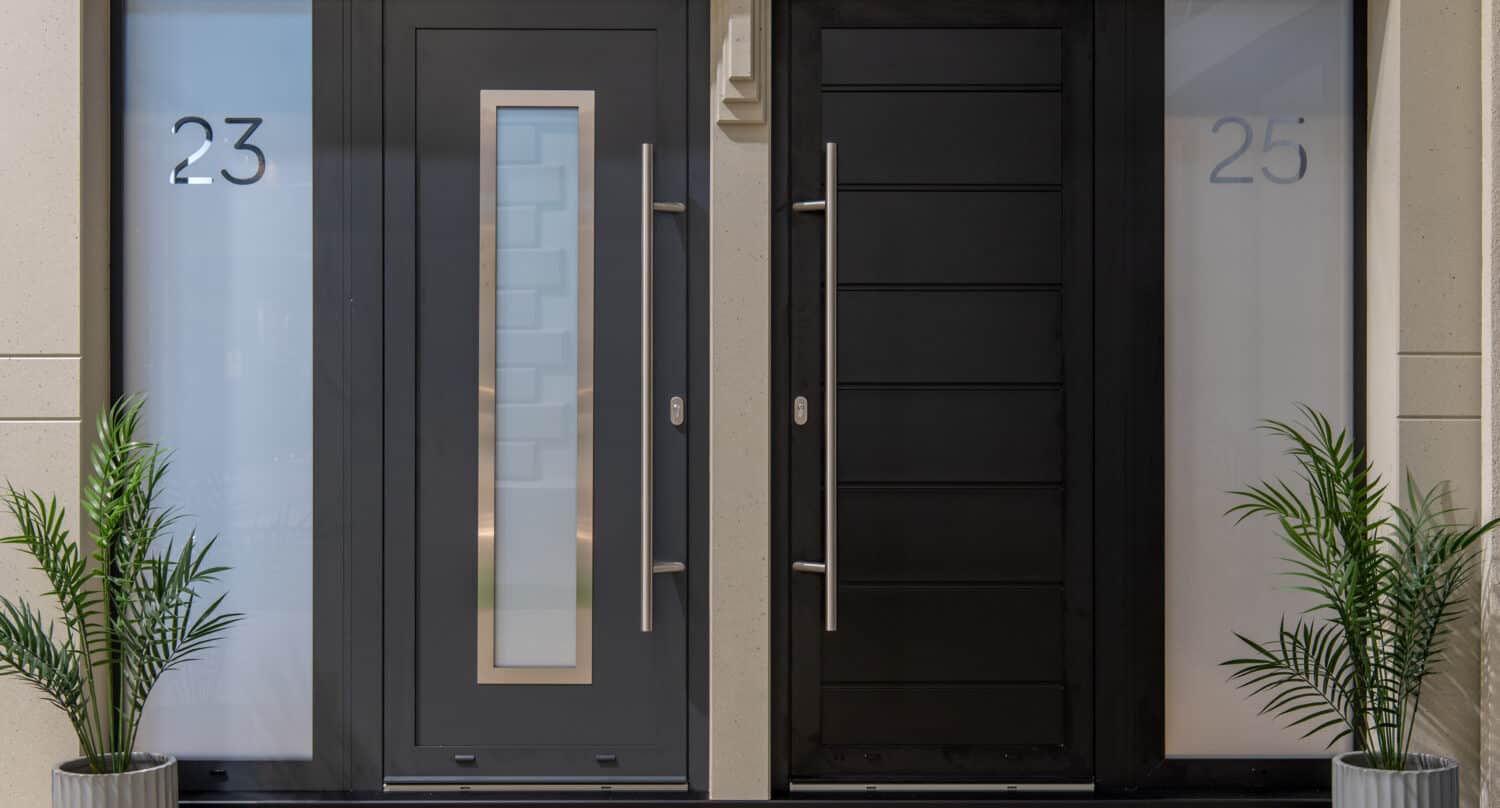 Two modern front doors—one gray with the number 23 and one black with 25—both feature tall silver handles, frosted side windows, and potted green plants, perfectly complementing homes with bespoke glass solutions or stylish glass roofing.