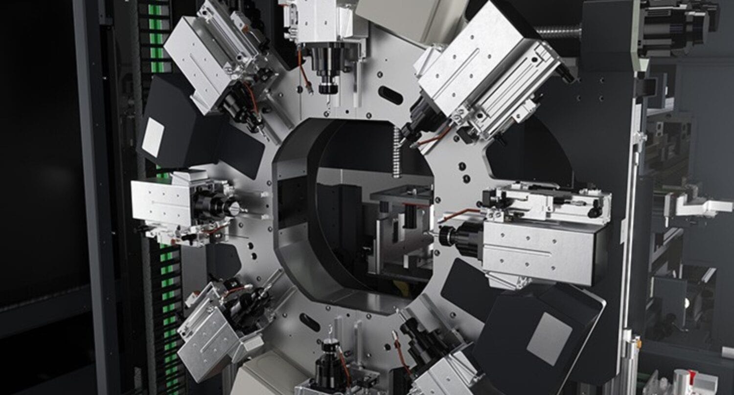 A close-up of an industrial machine with multiple robotic arms and components arranged in a circular pattern, featuring metallic parts, wires, and rectangular attachments for bespoke glass solutions inside a factory setting.