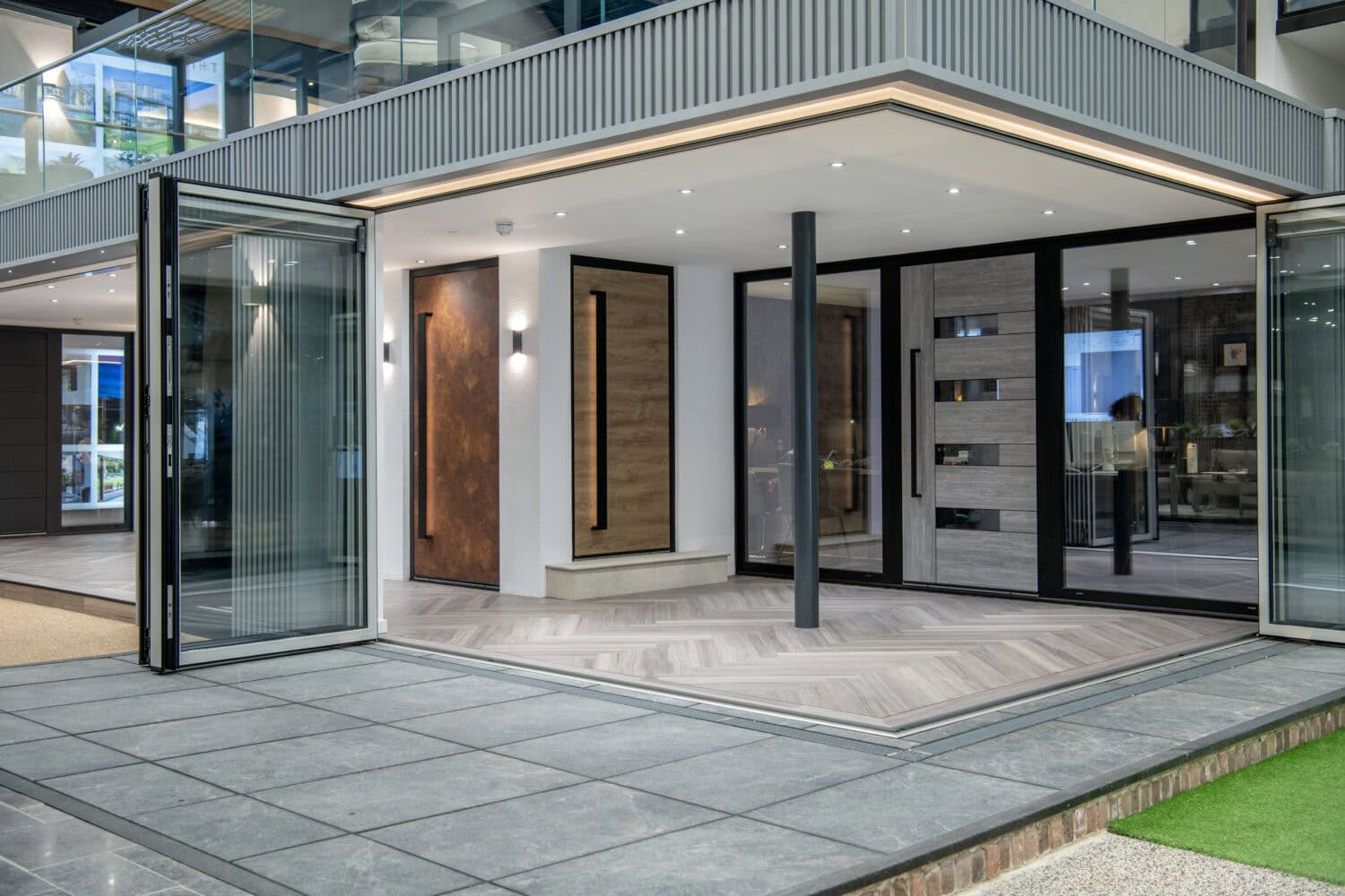 Modern home exterior with large bifold doors and glass roofing opens to a spacious indoor area featuring wood and tile floors, sleek paneling, and minimalist lighting, blending indoor and outdoor spaces seamlessly.