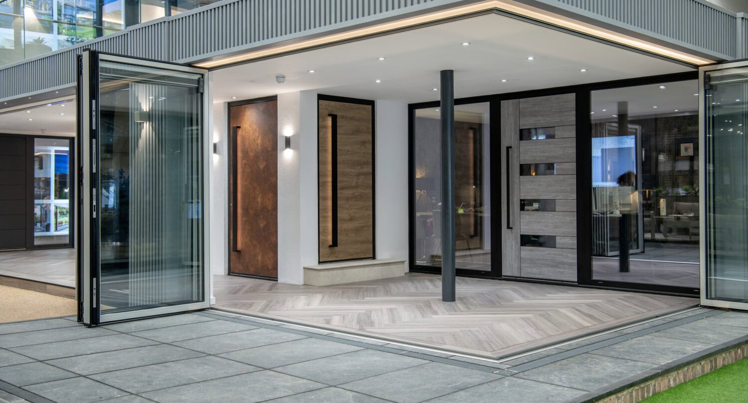 Modern home exterior with large bifold doors and glass roofing opens to a spacious indoor area featuring wood and tile floors, sleek paneling, and minimalist lighting, blending indoor and outdoor spaces seamlessly.