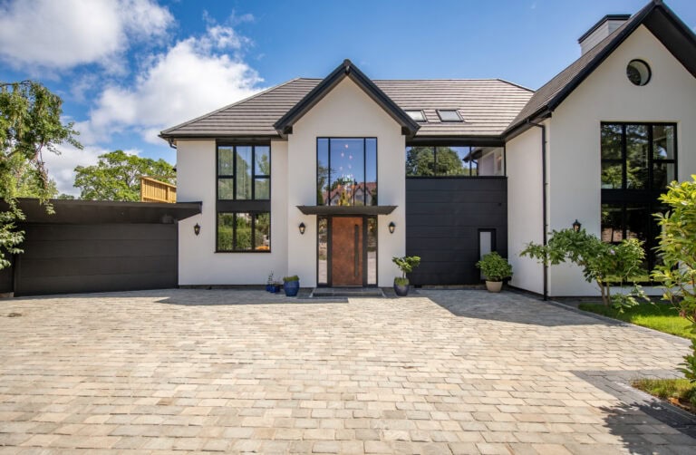 Modern house featuring large bi-folding doors with black frames and white exterior walls, set against a bright blue sky with greenery.