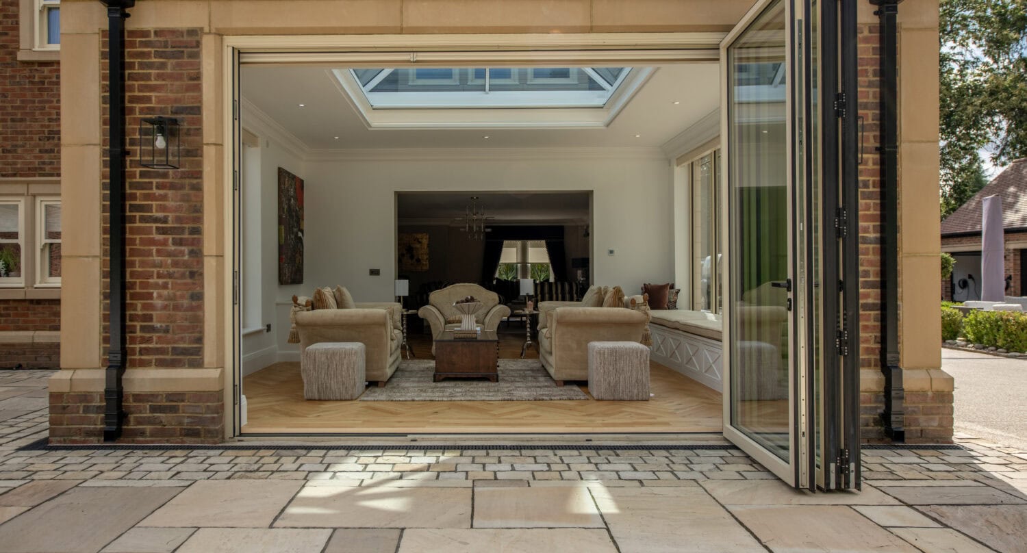 Modern bi-folding doors opening to a spacious, stylish living room with a skylight, creating seamless indoor-outdoor living space at Foxwood House.