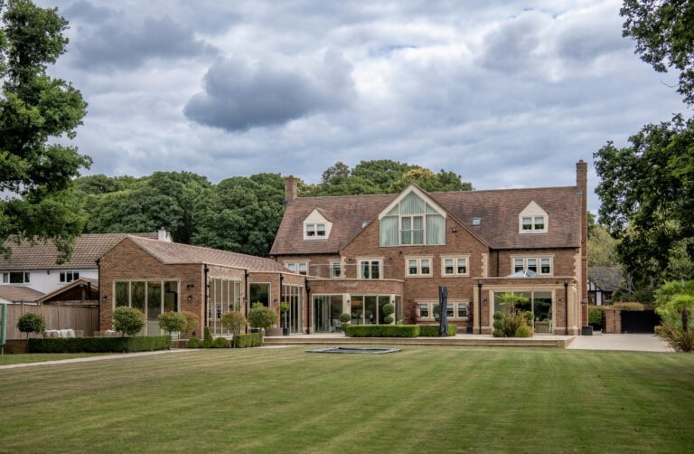 Large traditional brick house with modern bi-folding doors opening to a well-maintained garden and lawn.